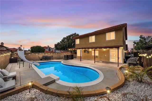 pool at dusk featuring a water slide and a patio