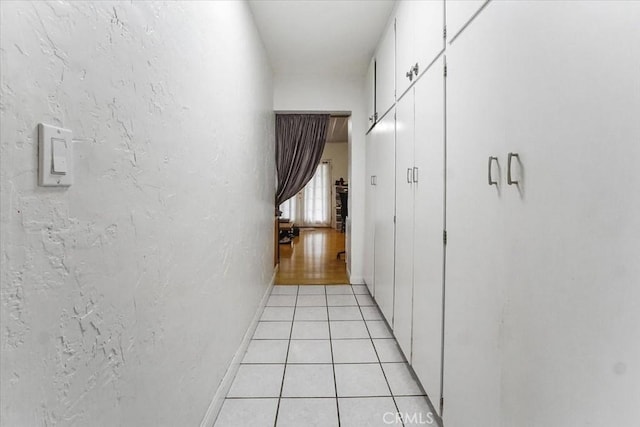 corridor with light tile patterned floors, a textured wall, and baseboards