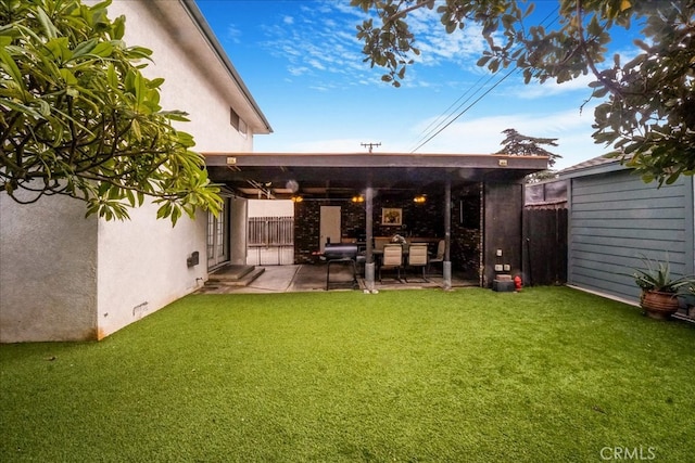 rear view of property with a patio area, a yard, fence, and stucco siding