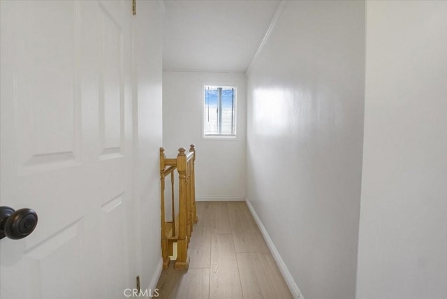 hall with light wood finished floors, baseboards, and an upstairs landing