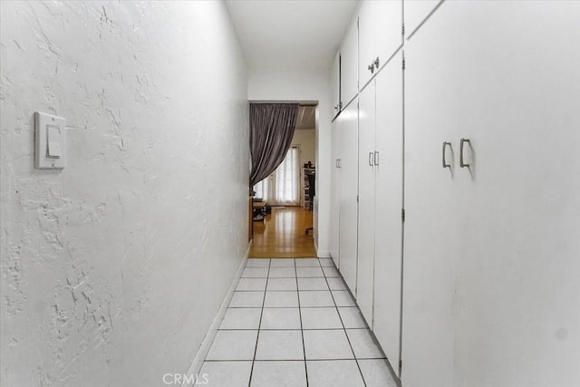 corridor featuring a textured wall, light tile patterned flooring, and baseboards