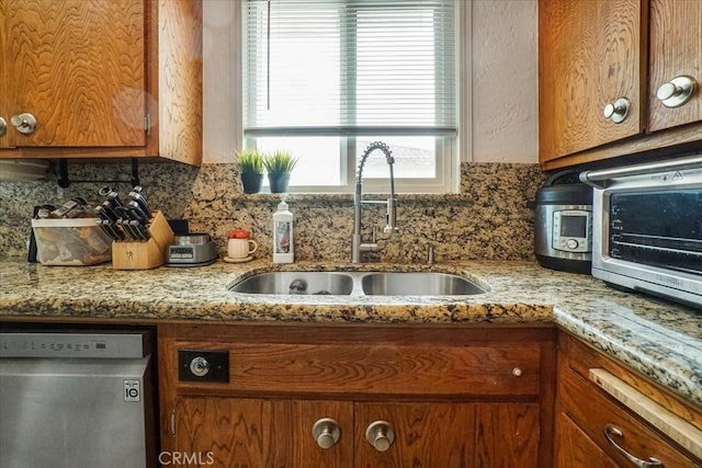 kitchen featuring brown cabinetry, dishwasher, a sink, and tasteful backsplash