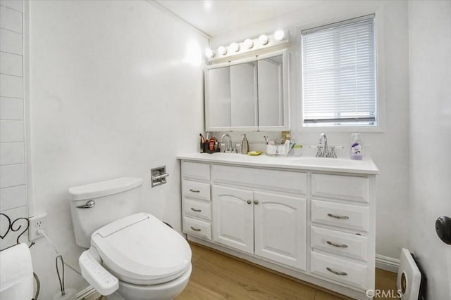 full bathroom with toilet, double vanity, a sink, and wood finished floors