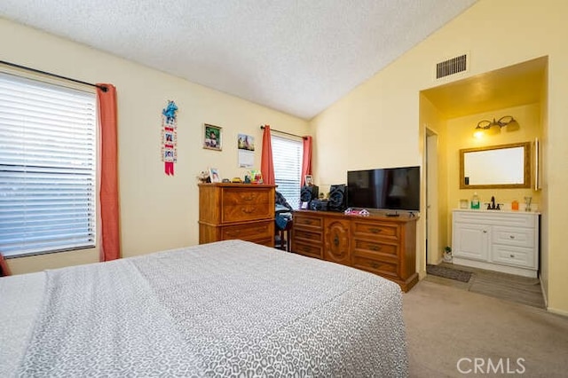 carpeted bedroom with vaulted ceiling, a textured ceiling, and ensuite bath