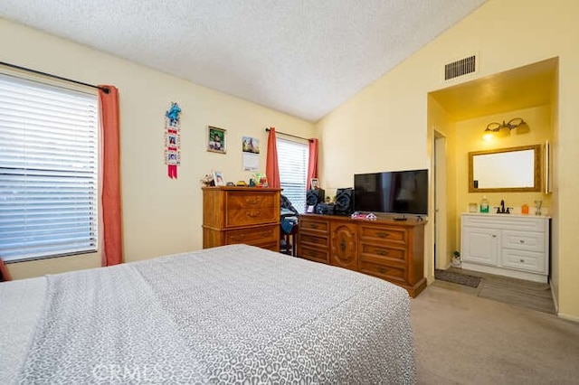 carpeted bedroom with visible vents, vaulted ceiling, a textured ceiling, and ensuite bathroom