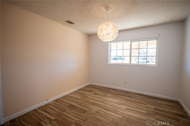 unfurnished room featuring hardwood / wood-style flooring, a notable chandelier, and a textured ceiling