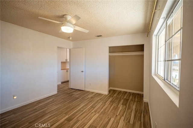 unfurnished bedroom with a textured ceiling, hardwood / wood-style flooring, a closet, and ceiling fan