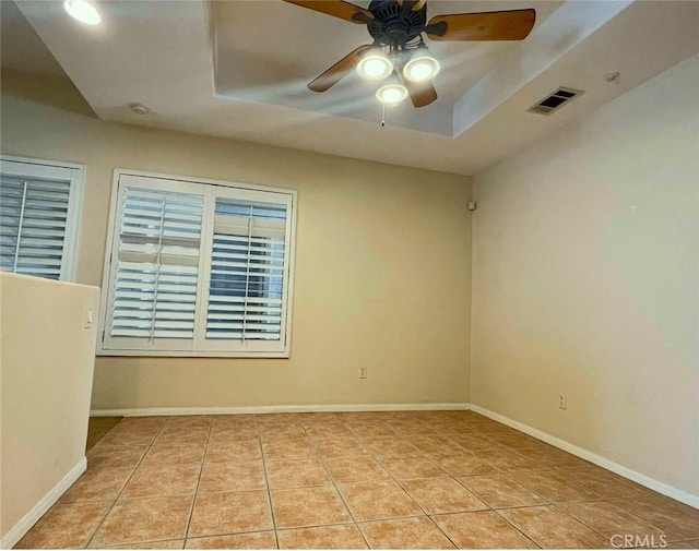 tiled spare room featuring a raised ceiling and ceiling fan