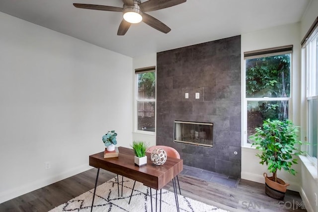 home office featuring wood-type flooring, ceiling fan, a healthy amount of sunlight, and a tiled fireplace