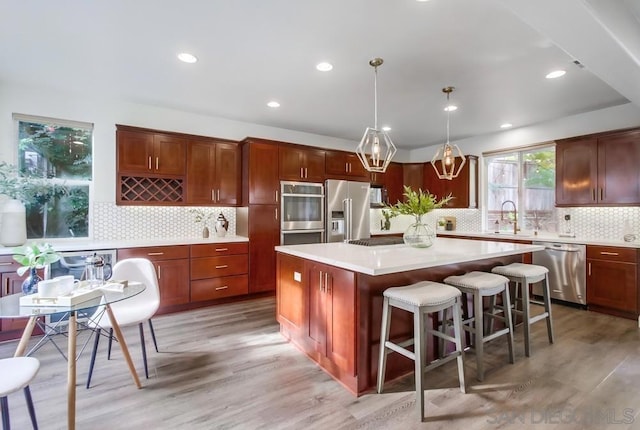 kitchen with appliances with stainless steel finishes, backsplash, pendant lighting, a center island, and light hardwood / wood-style floors