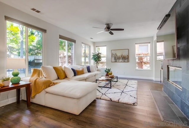 living room featuring a wealth of natural light, a fireplace, ceiling fan, and dark hardwood / wood-style floors