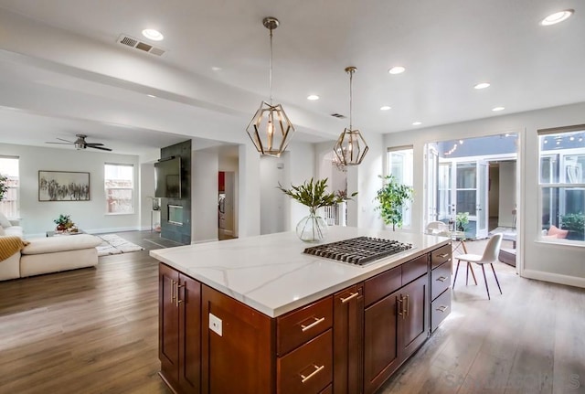 kitchen with a center island, hanging light fixtures, light stone counters, wood-type flooring, and ceiling fan with notable chandelier