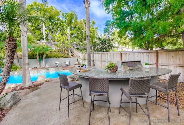 view of patio with area for grilling, a fenced in pool, and an outdoor bar