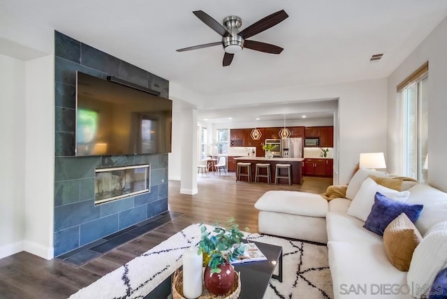 living room with dark hardwood / wood-style flooring, ceiling fan, and a tiled fireplace