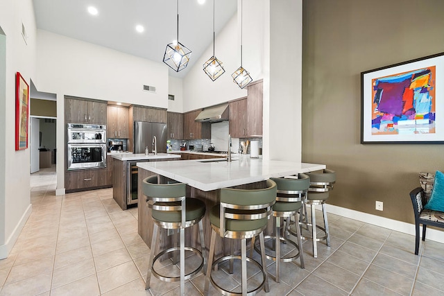 kitchen with a breakfast bar, high vaulted ceiling, wall chimney exhaust hood, decorative light fixtures, and kitchen peninsula