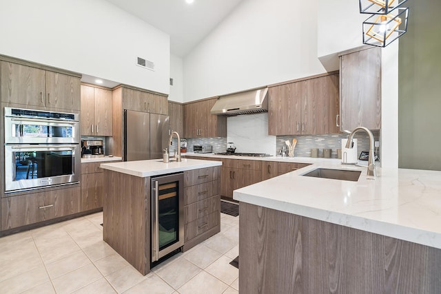 kitchen with pendant lighting, high vaulted ceiling, wall chimney range hood, wine cooler, and stainless steel appliances