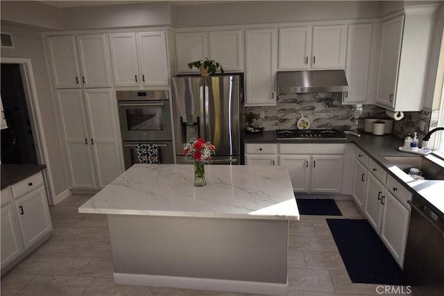 kitchen with appliances with stainless steel finishes, a center island, light stone countertops, white cabinets, and sink