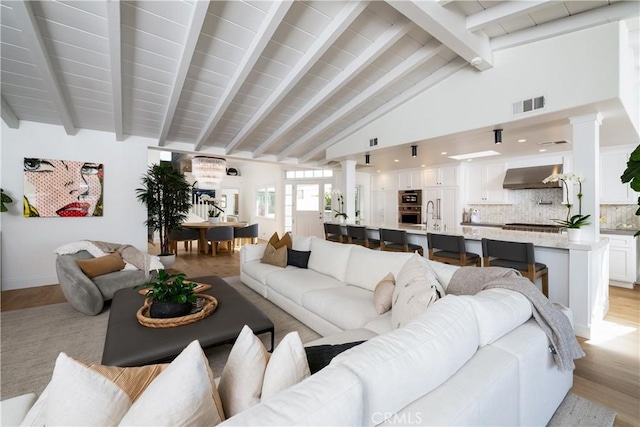 living room with beam ceiling, light wood-type flooring, and high vaulted ceiling