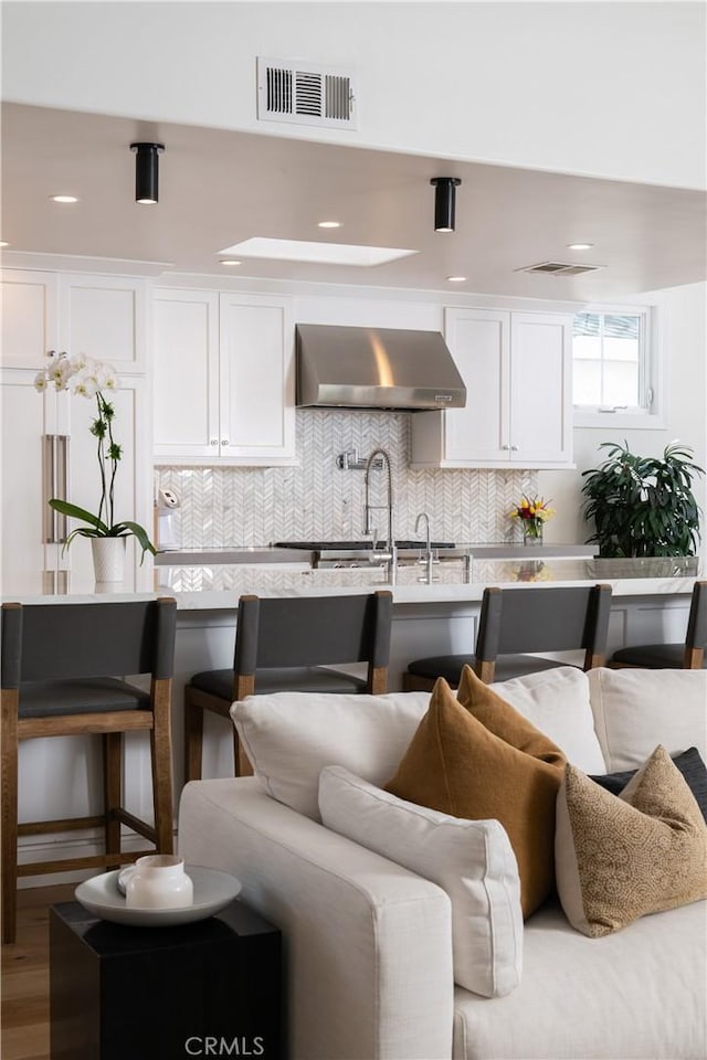 kitchen with decorative backsplash, white cabinetry, and wall chimney exhaust hood