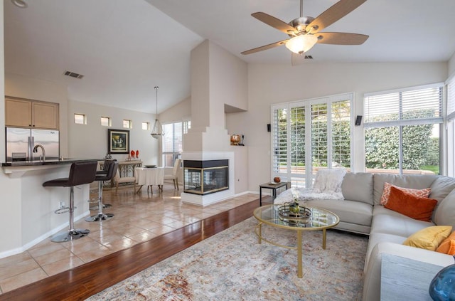 living room with ceiling fan, light wood-type flooring, a multi sided fireplace, lofted ceiling, and sink