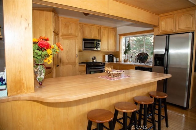 kitchen featuring stainless steel appliances, a kitchen breakfast bar, tasteful backsplash, kitchen peninsula, and light brown cabinets