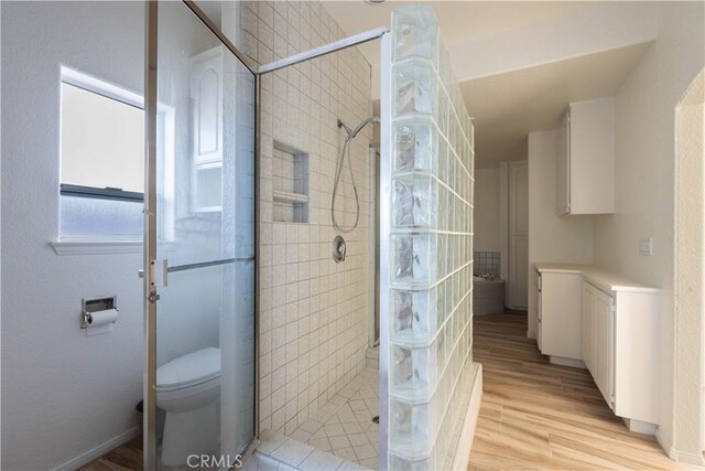 bathroom with toilet, wood finished floors, and a tile shower