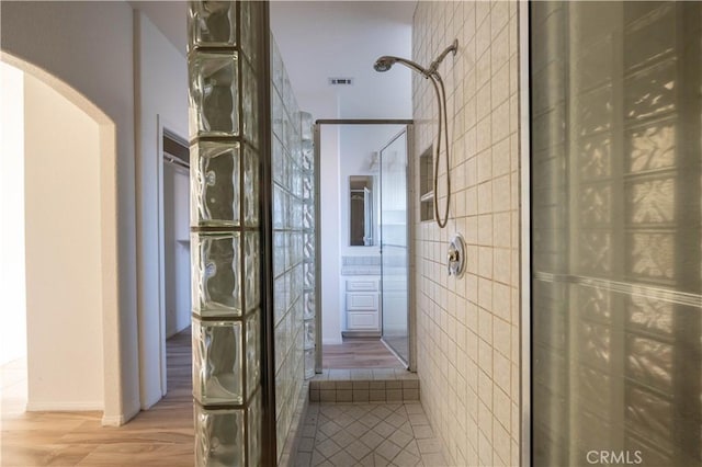 full bathroom featuring visible vents, tiled shower, tile walls, and wood finished floors