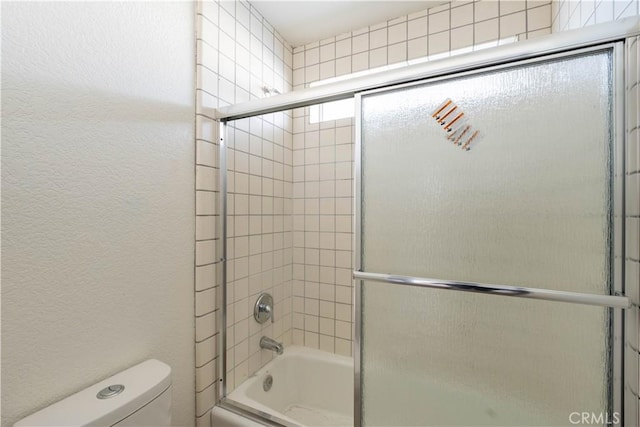 full bath with toilet, a textured wall, and bath / shower combo with glass door