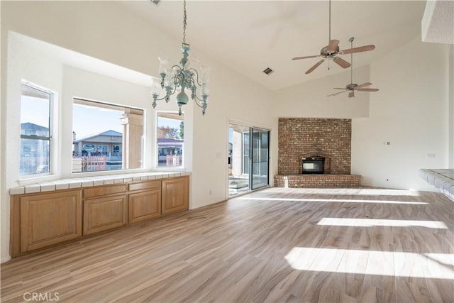 unfurnished living room featuring visible vents, a brick fireplace, light wood-style flooring, an inviting chandelier, and high vaulted ceiling