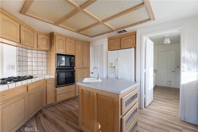 kitchen with black appliances, light wood-style flooring, an island with sink, a sink, and tile countertops