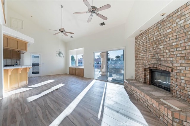 unfurnished living room featuring visible vents, a fireplace, high vaulted ceiling, and light wood-type flooring