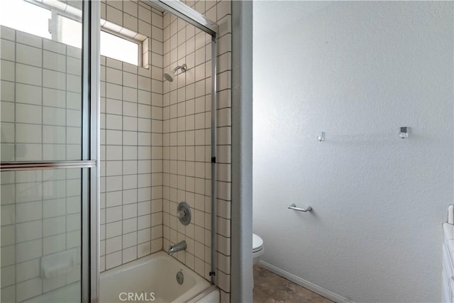 bathroom with toilet, a textured wall, baseboards, and shower / bath combination with glass door