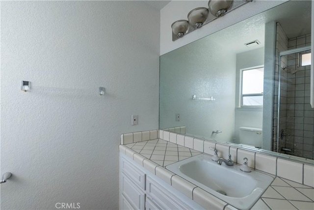 bathroom with visible vents, tiled shower, vanity, and a textured wall