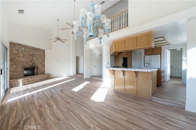 kitchen featuring visible vents, a brick fireplace, tile counters, light wood-type flooring, and white fridge with ice dispenser