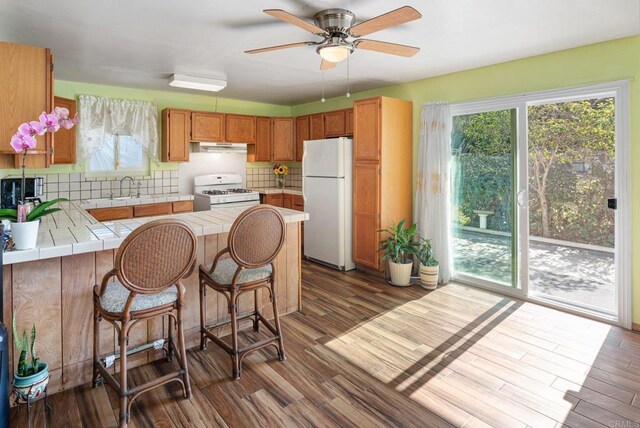 kitchen with dark hardwood / wood-style flooring, backsplash, white appliances, and tile countertops