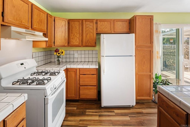 kitchen featuring backsplash, white appliances, tile counters, and dark wood-type flooring