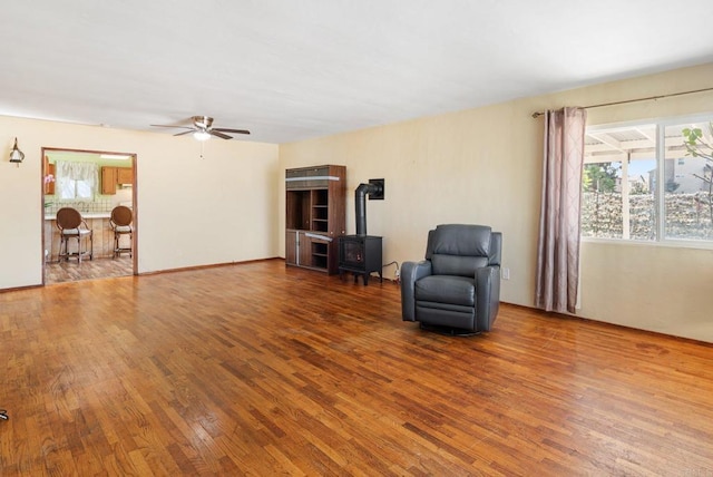 sitting room featuring hardwood / wood-style flooring, ceiling fan, and a wood stove