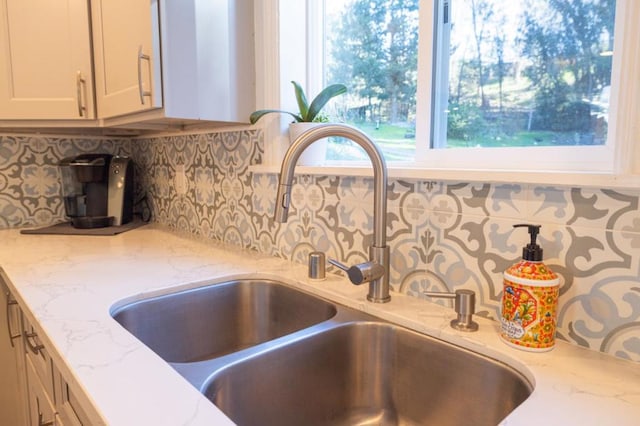 room details featuring white cabinetry, sink, tasteful backsplash, and light stone countertops