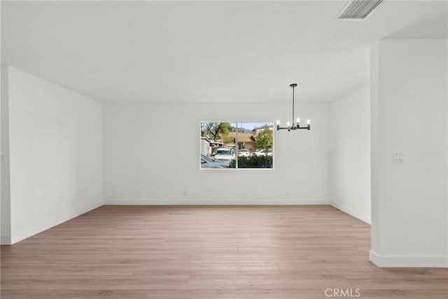 spare room featuring light hardwood / wood-style floors and a notable chandelier