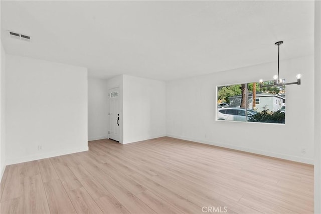 empty room featuring light wood-type flooring and an inviting chandelier