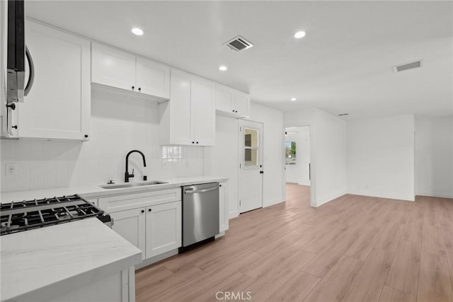 kitchen featuring white cabinetry, sink, light stone counters, stainless steel dishwasher, and light hardwood / wood-style floors