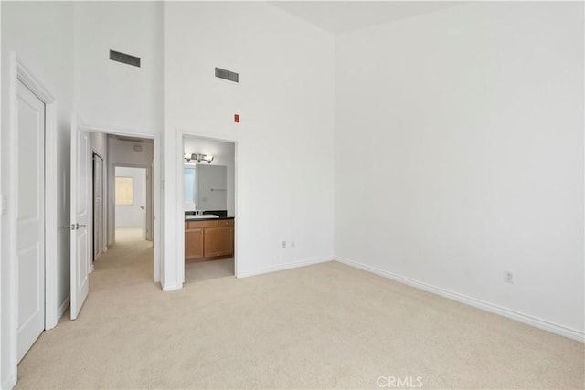 unfurnished bedroom with light carpet, a towering ceiling, ensuite bathroom, and sink