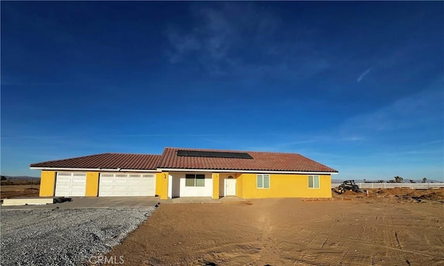 view of front of house featuring stucco siding, a tiled roof, an attached garage, and solar panels