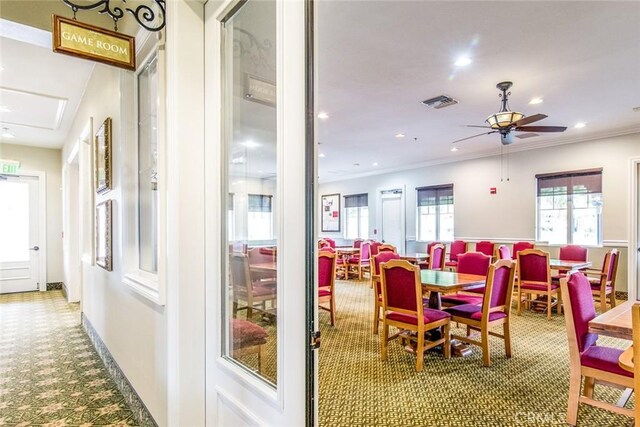 carpeted dining space featuring ceiling fan and crown molding