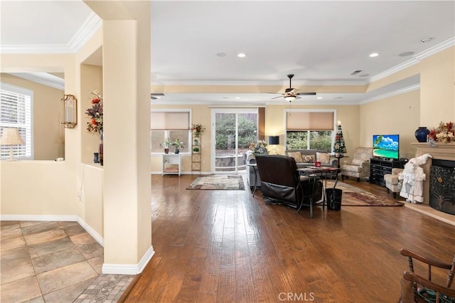 living area with ornamental molding, ceiling fan, a warm lit fireplace, baseboards, and hardwood / wood-style flooring