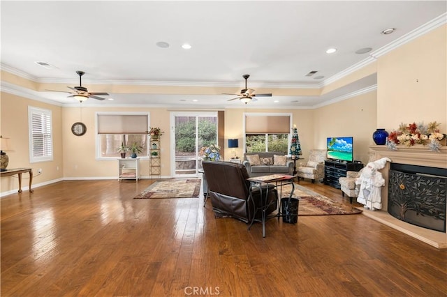 living area with hardwood / wood-style flooring, ornamental molding, a fireplace with raised hearth, and a ceiling fan