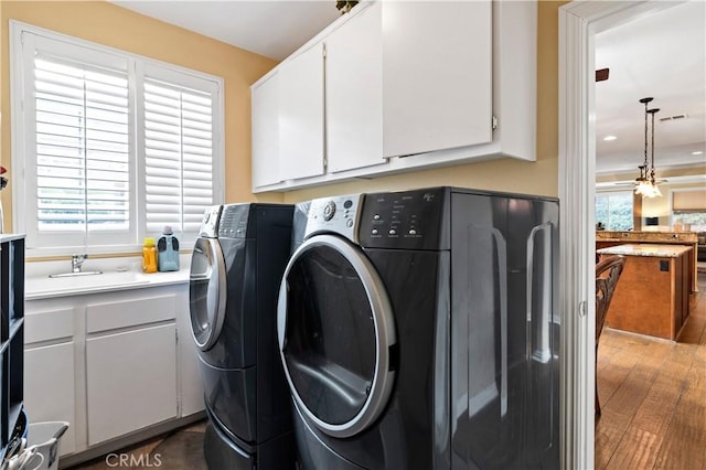 laundry area featuring cabinet space, visible vents, wood finished floors, washing machine and clothes dryer, and a sink