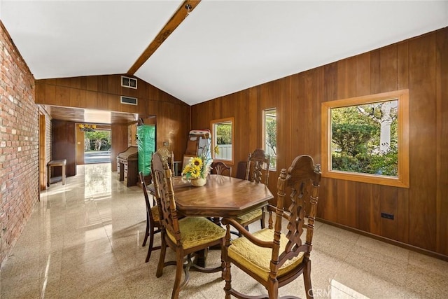 dining room with wood walls, lofted ceiling with beams, and a healthy amount of sunlight