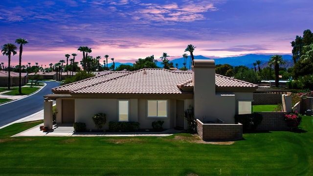 back house at dusk with a mountain view and a lawn