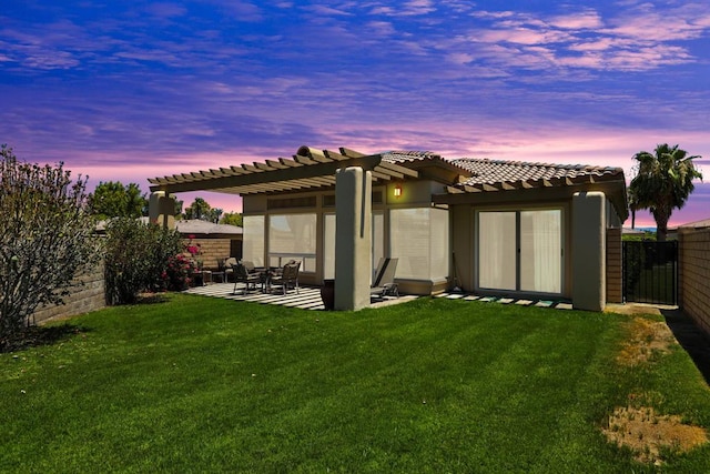 back house at dusk featuring a pergola, a patio area, and a lawn